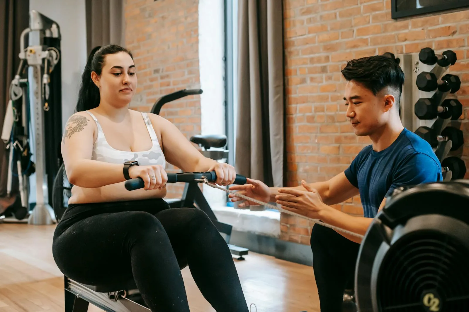Woman practising rowing machine technique with personal trainer guidance