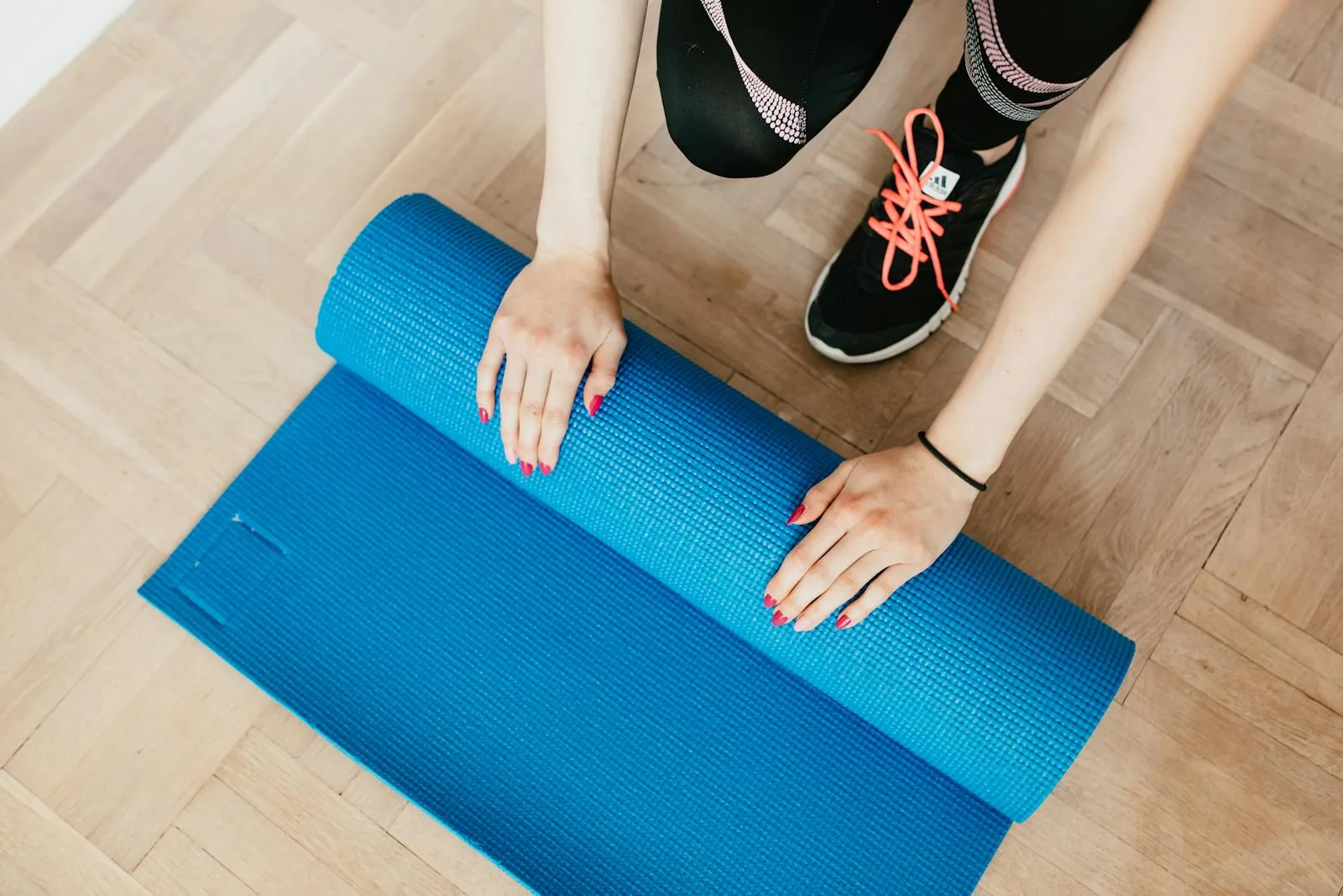 Person rolling up blue yoga mat on wooden floor after home workout
